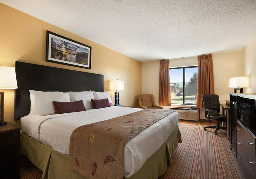 standard king room with bed across from dresser with microwave at Ramada by Wyndham Wisconsin Dells